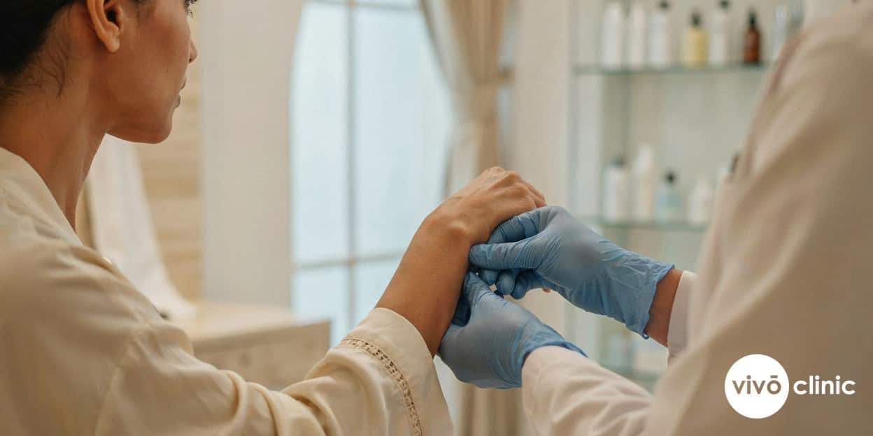 Practitioner in modest attire gently assessing the skin elasticity on the back of a Middle Eastern woman’s upper arm before fat dissolving treatment at VIVO Clinic Dubai
