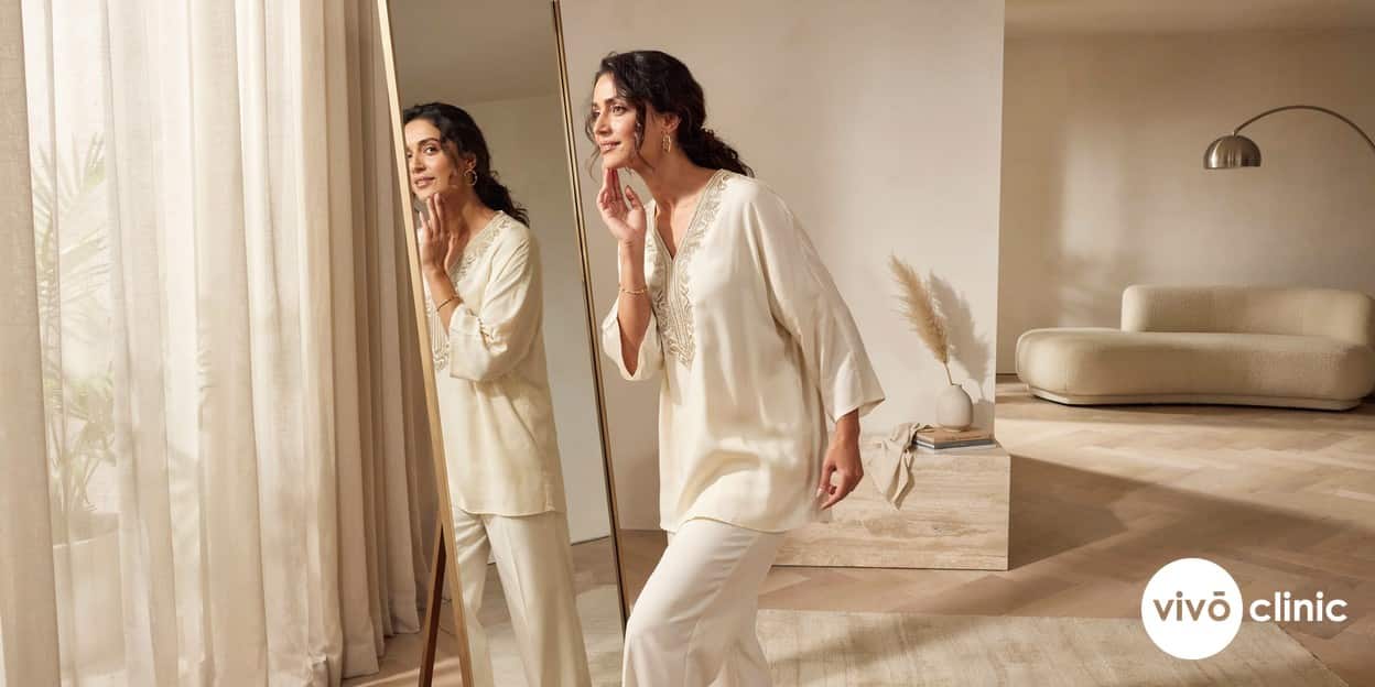 Middle Eastern woman admiring her slimmer, more defined jawline in a mirror after double chin treatment, in a premium home setting