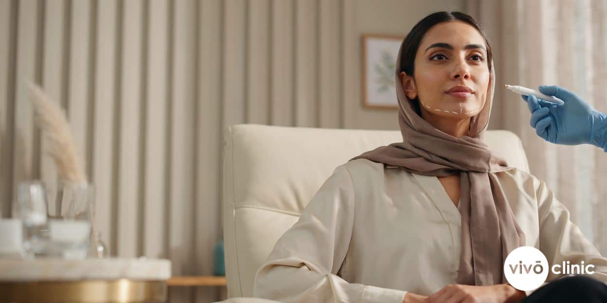 Middle Eastern woman with white cosmetic marking lines beneath her chin during a double chin consultation at VIVO Clinic Dubai, comparing Aqualyx and fat freezing