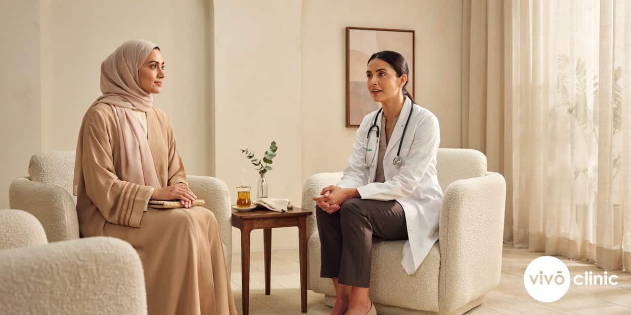 Reassuring Middle Eastern woman in modest dress in conversation with a female doctor in a calm, premium consultation room at VIVO Clinic Dubai, discussing post-partum recovery, no device, machine or handpiece anywhere in frame