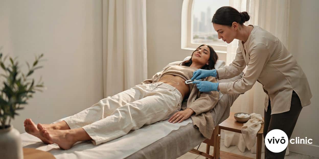 Practitioner in modest attire using calipers to assess a small pocket of fat marked with white lines on a Middle Eastern woman’s abdomen at VIVO Clinic Dubai