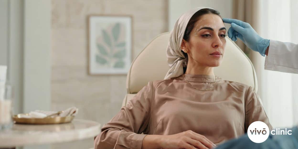 Middle Eastern woman with white cosmetic marking lines above her lateral eyebrow during a non-surgical HIFU brow lift consultation at VIVO Clinic Dubai