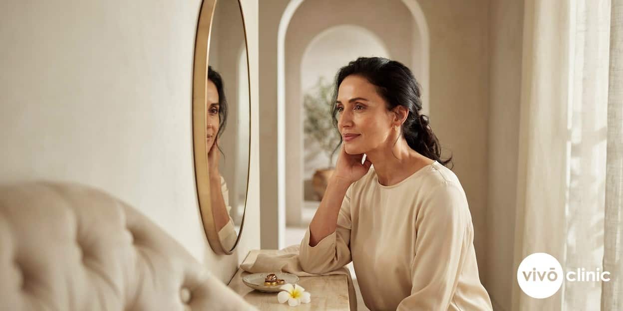 Middle Eastern woman smiling as she studies her firmer, more defined jawline in a mirror after HIFU jowl treatment in a premium Dubai clinic