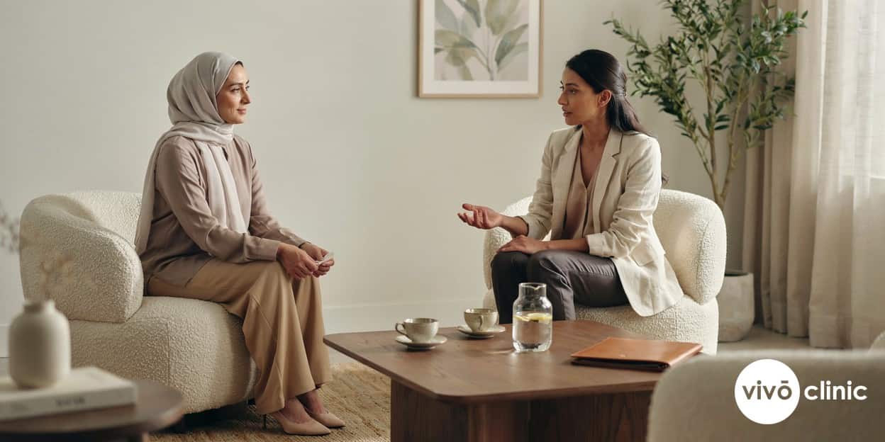 Reassured Middle Eastern woman in her fifties in modest clothing talking with a female practitioner in a calm, private consultation room at VIVO Clinic Dubai, conveying confidentiality and comfort, no device or machine in frame