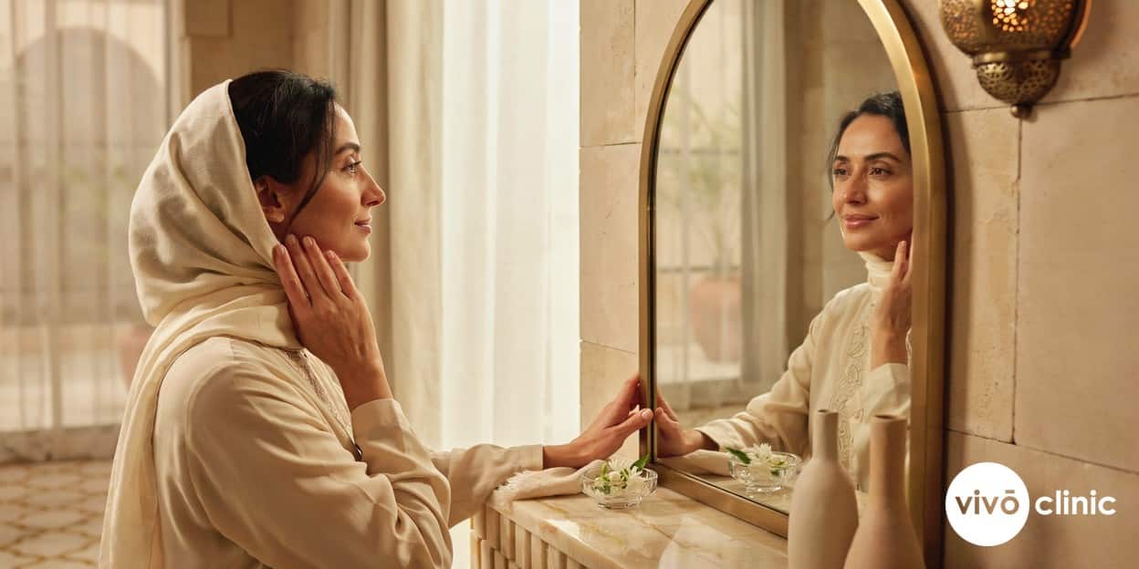 Middle Eastern woman examining her firmer, more defined jawline in a mirror after combined HIFU and RF skin tightening at VIVO Clinic Dubai