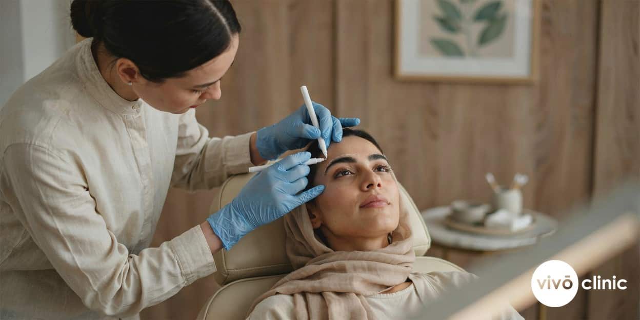 Practitioner in modest attire using white cosmetic marking pen to map fine lines around a Middle Eastern woman’s eye before a plasma fibroblast assessment at VIVO Clinic Dubai