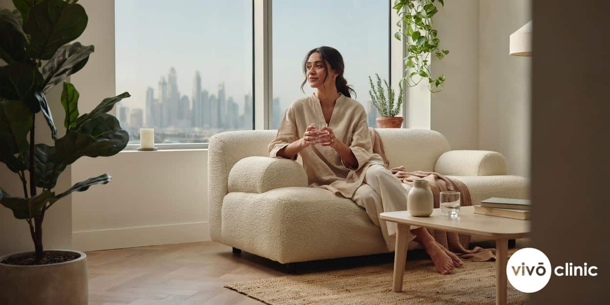 Middle Eastern woman in comfortable modest clothing relaxing calmly at home with a glass of water, conveying wellbeing and recovery after a non-surgical intimate HIFU treatment