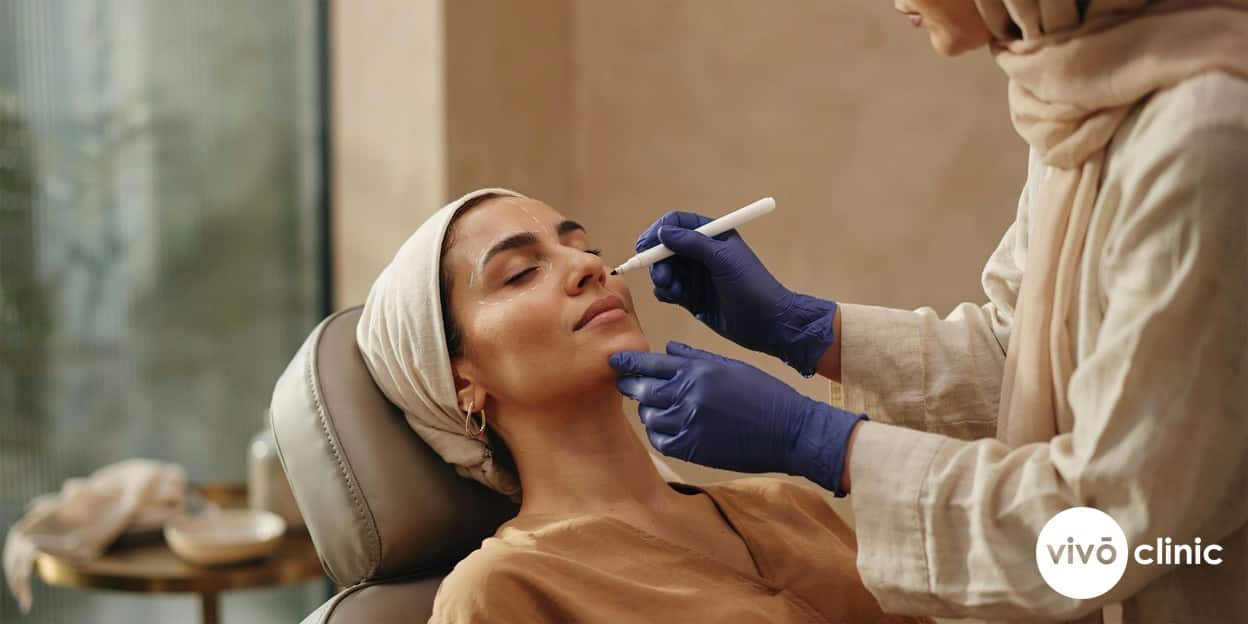 Practitioner in modest attire marking white assessment lines along a Middle Eastern woman’s cheek while planning an RF facelift maintenance schedule at VIVO Clinic Dubai
