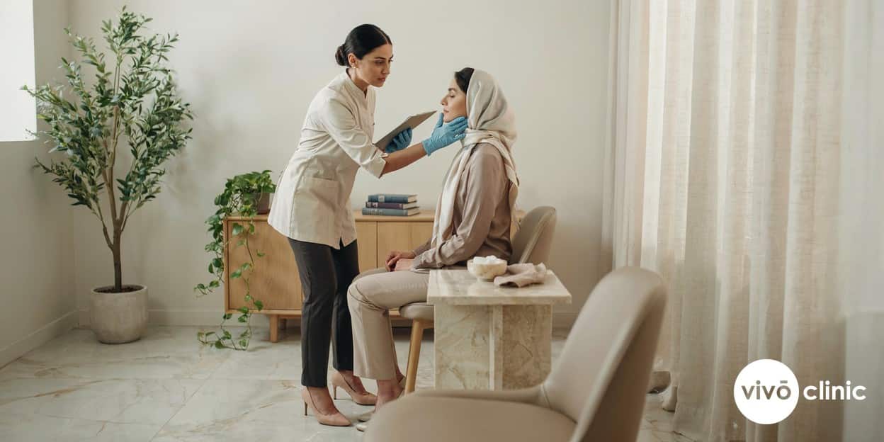 Practitioner in modest attire reviewing a Middle Eastern woman’s jawline and lower face at a follow-up assessment, planning whether a maintenance HIFU session is needed, in a premium Dubai clinic with no device in frame