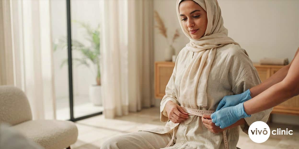 Middle Eastern woman in modest dress having her waistline measured with a tape measure during an ultrasound cavitation planning consultation at VIVO Clinic Dubai