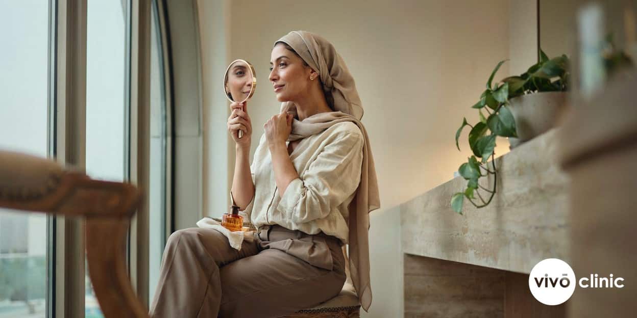 Middle Eastern woman examining her smoother, firmer cheek and jawline in a mirror after a radiofrequency skin tightening course at VIVO Clinic Dubai