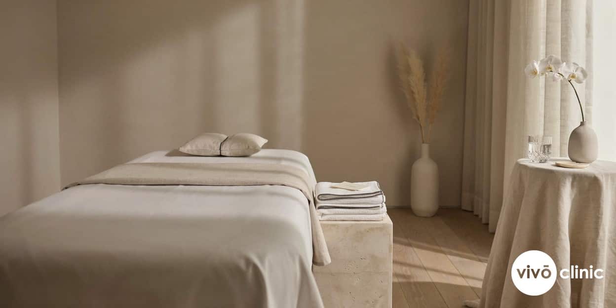 Photorealistic still-life of a serene, premium Dubai clinic treatment room with soft neutral linens, a covered treatment couch and warm private lighting, conveying discretion and calm