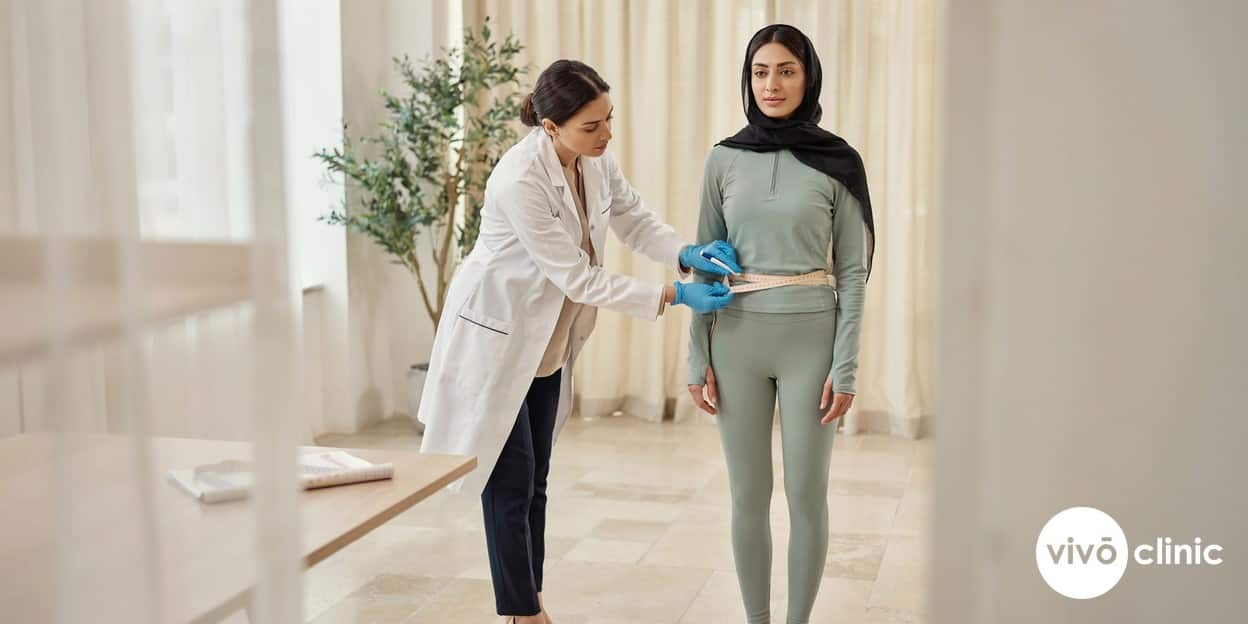 Practitioner in modest attire using a tape measure and white marking pen to assess a Middle Eastern woman’s waistline before non-surgical body contouring at VIVO Clinic Dubai, no device, machine or handpiece anywhere in frame