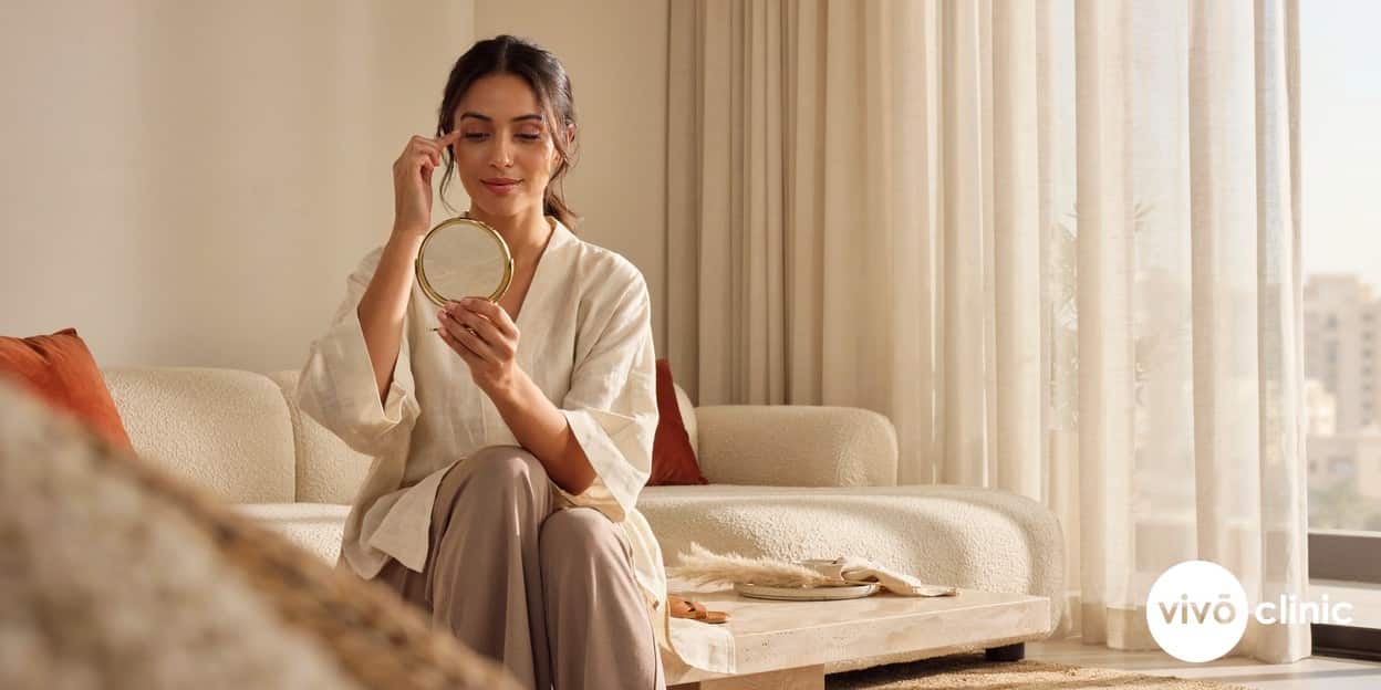 Middle Eastern woman in modest dress examining her more open, lifted upper eyelids in a hand mirror after a plasma eye lift for hooded eyelids at VIVO Clinic Dubai