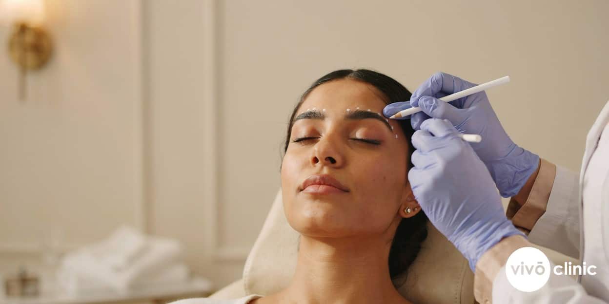 Practitioner in modest attire using fine white marking dots to assess a Middle Eastern woman’s mild upper-eyelid hooding before a plasma eye lift at VIVO Clinic Dubai