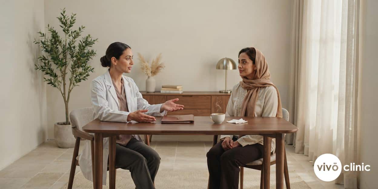 Middle Eastern woman in modest dress in a calm, private consultation room at VIVO Clinic Dubai, speaking with a female practitioner across a desk
