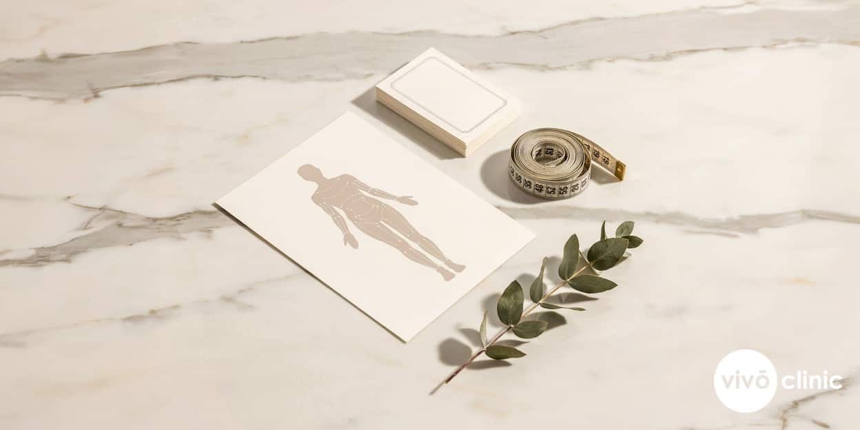 Comparison still-life on a clean clinic surface showing white cosmetic marking lines on a body outline diagram, a tape measure and treatment record cards representing different non-surgical fat reduction options