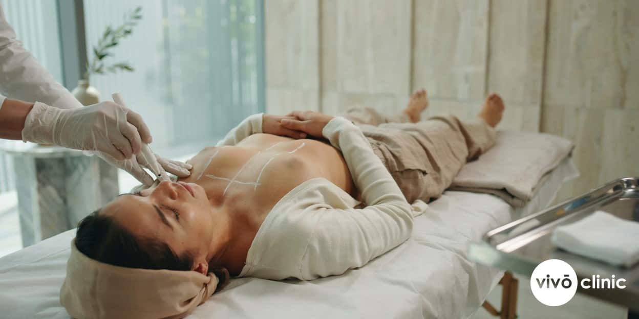 Practitioner in modest attire wearing gloves drawing white marking lines on a Middle Eastern woman’s abdomen before ultrasound cavitation at VIVO Clinic Dubai, no device in frame