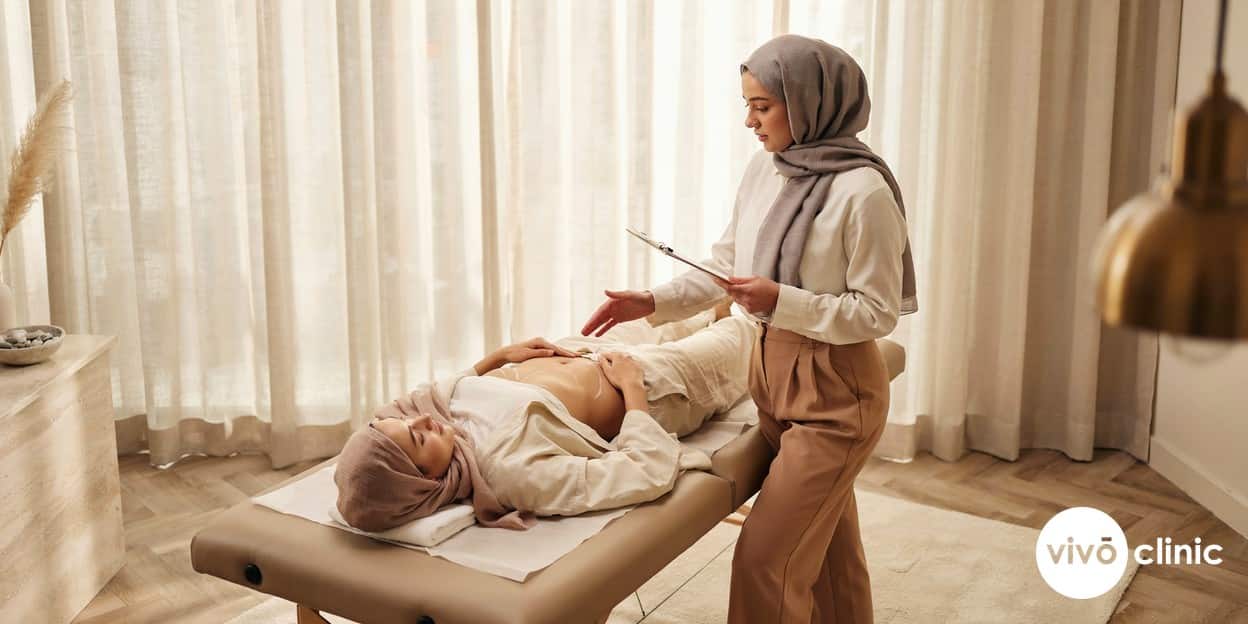 Middle Eastern woman in modest dress relaxing during an ultrasound cavitation body contouring consultation at VIVO Clinic Dubai, with white marking lines on her abdomen