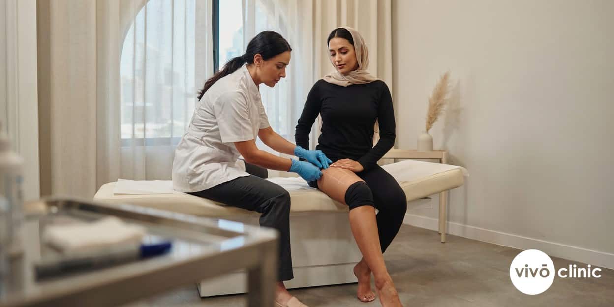 Practitioner in modest attire wearing gloves, using a pinch test to assess cellulite grade on a Middle Eastern woman’s thigh at VIVO Clinic Dubai, with white cosmetic marking lines indicating treatment zones