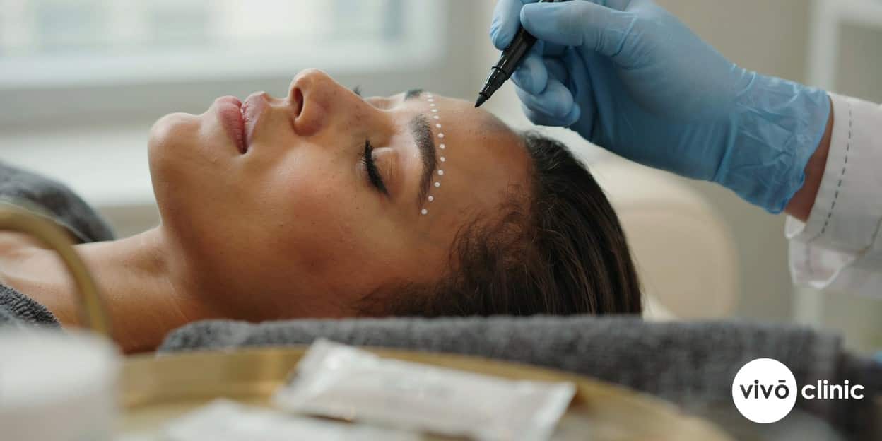 Practitioner in modest attire using fine white cosmetic dots to map a treatment grid across a Middle Eastern woman’s upper eyelid before a non-surgical plasma eye lift, no device, machine or handpiece anywhere in frame