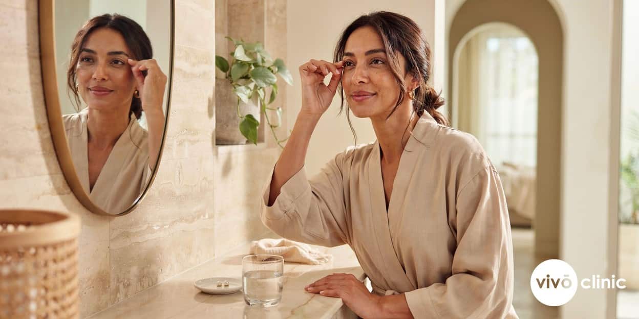 Middle Eastern woman gently examining her smoother, firmer upper eyelids in a mirror three months after a plasma eye lift at VIVO Clinic Dubai