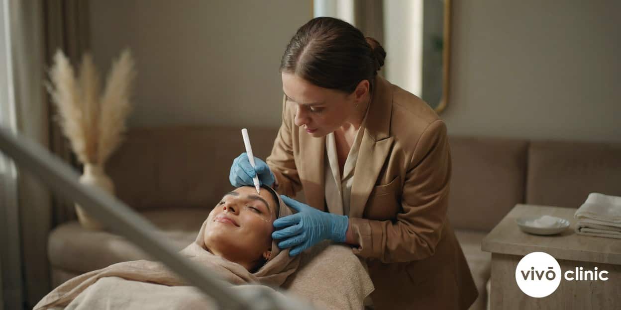 Practitioner in modest attire drawing white cosmetic treatment-mapping lines across the cheek of a Middle Eastern woman during an RF facelift assessment, no device, machine or handpiece anywhere in frame