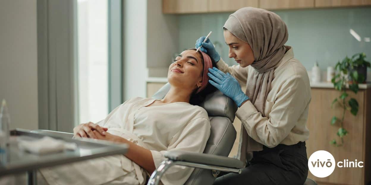 Practitioner in modest attire marking white cosmetic assessment lines along a Middle Eastern woman’s cheek and jawline before HIFU treatment at VIVO Clinic Dubai
