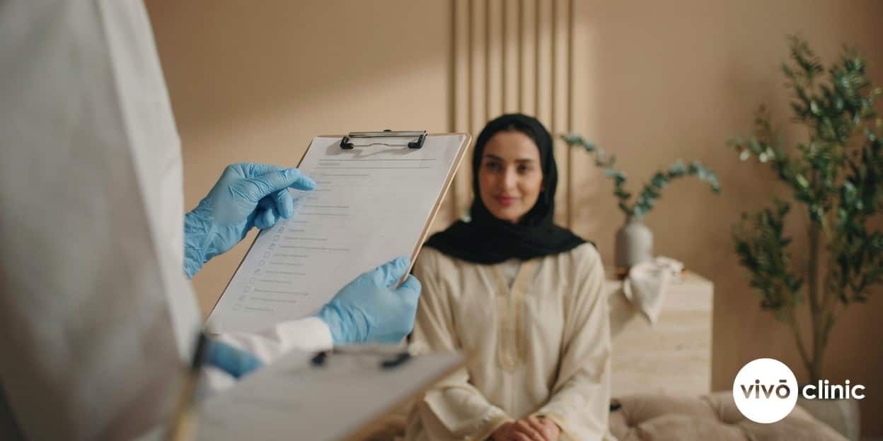 Practitioner’s gloved hands holding a clipboard reviewing a HIFU skin tightening suitability checklist beside a relaxed Middle Eastern client in a calm, premium Dubai clinic room, no device, machine or handpiece anywhere in frame