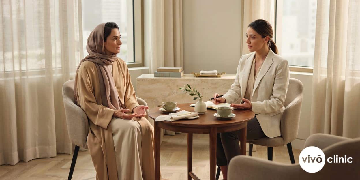 Middle Eastern woman in modest attire in a calm consultation room at VIVO Clinic Dubai discussing plasma eye lift suitability with a practitioner, no device, machine or handpiece anywhere in frame