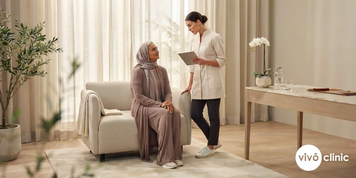 Practitioner in modest attire holding a tablet and reviewing a medical-history checklist with a Middle Eastern woman to screen for Aqualyx contraindications, no device, machine or handpiece anywhere in frame